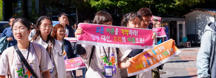 모든 이름을 기억하라, 장애 대신 우리의 이름으로라고 적힌 현수막을 들고 행진하는 참가자들